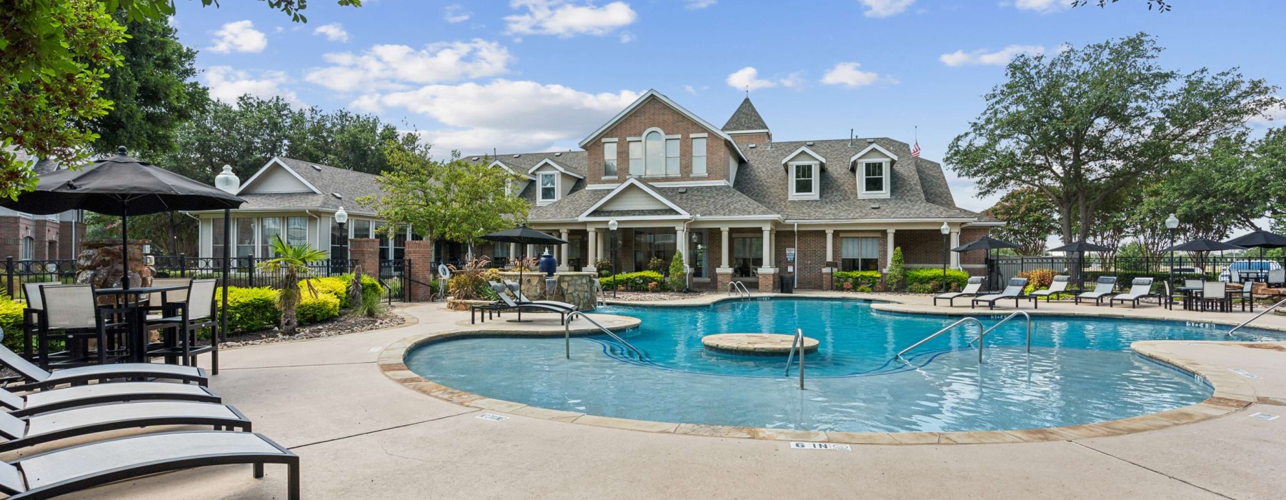 Resort-style pool at Villas at Legacy apartments in Plano, TX, with lush greenery, water features, and lounge seating