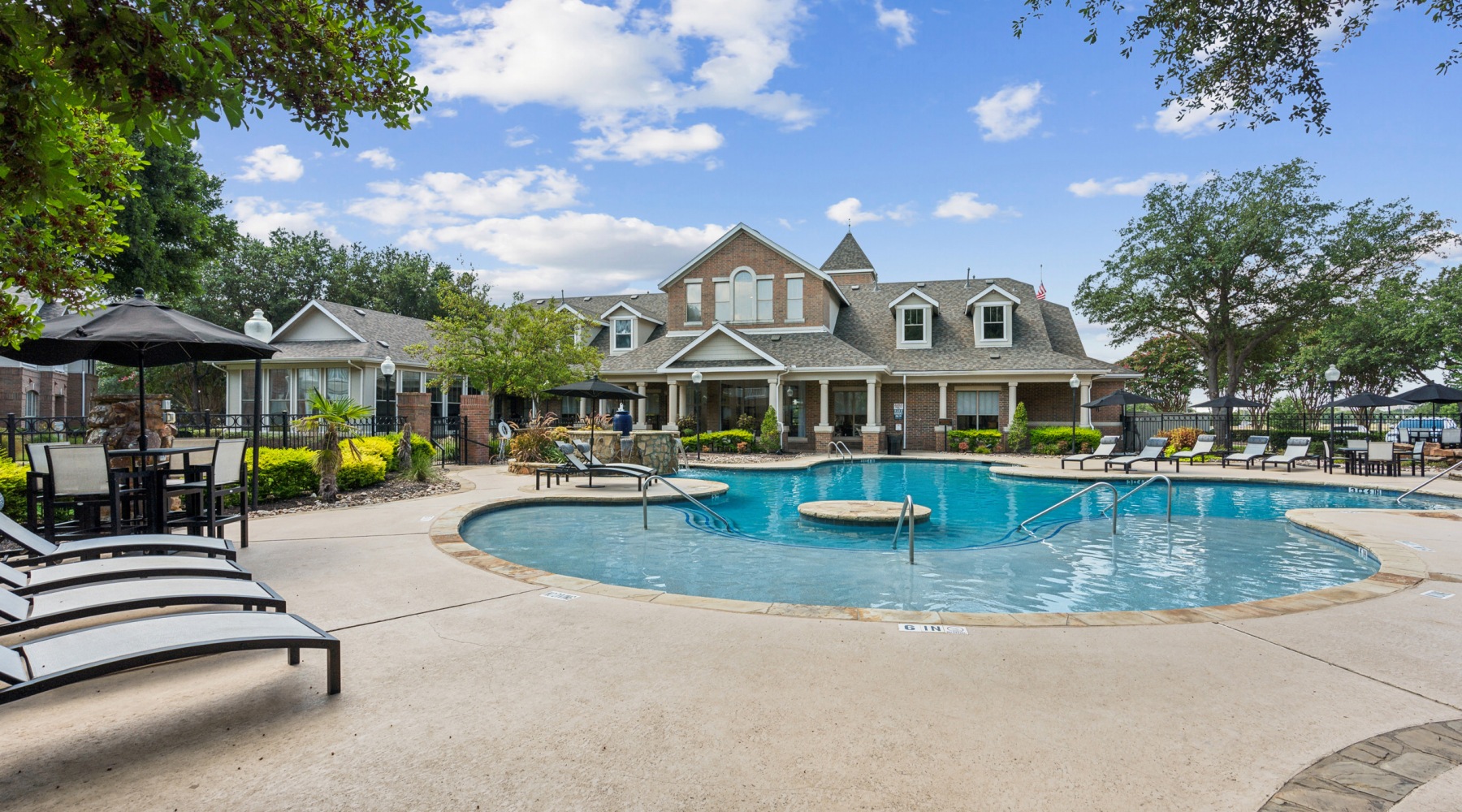 Resort-style pool at Villas at Legacy apartments in Plano, TX, with lush greenery, water features, and lounge seating